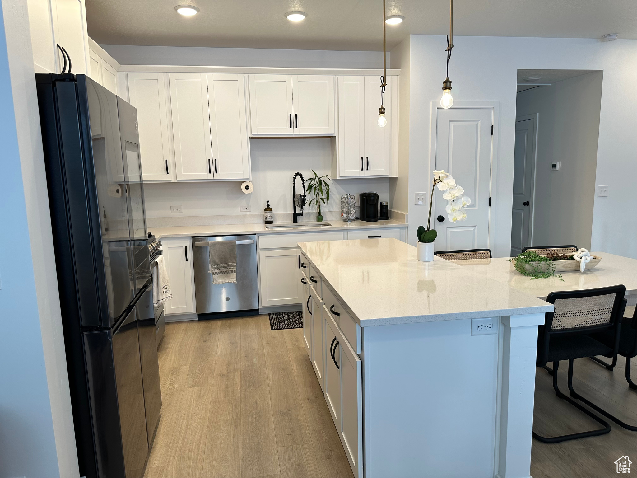 Kitchen with black refrigerator, hanging light fixtures, white cabinetry, and stainless steel dishwasher