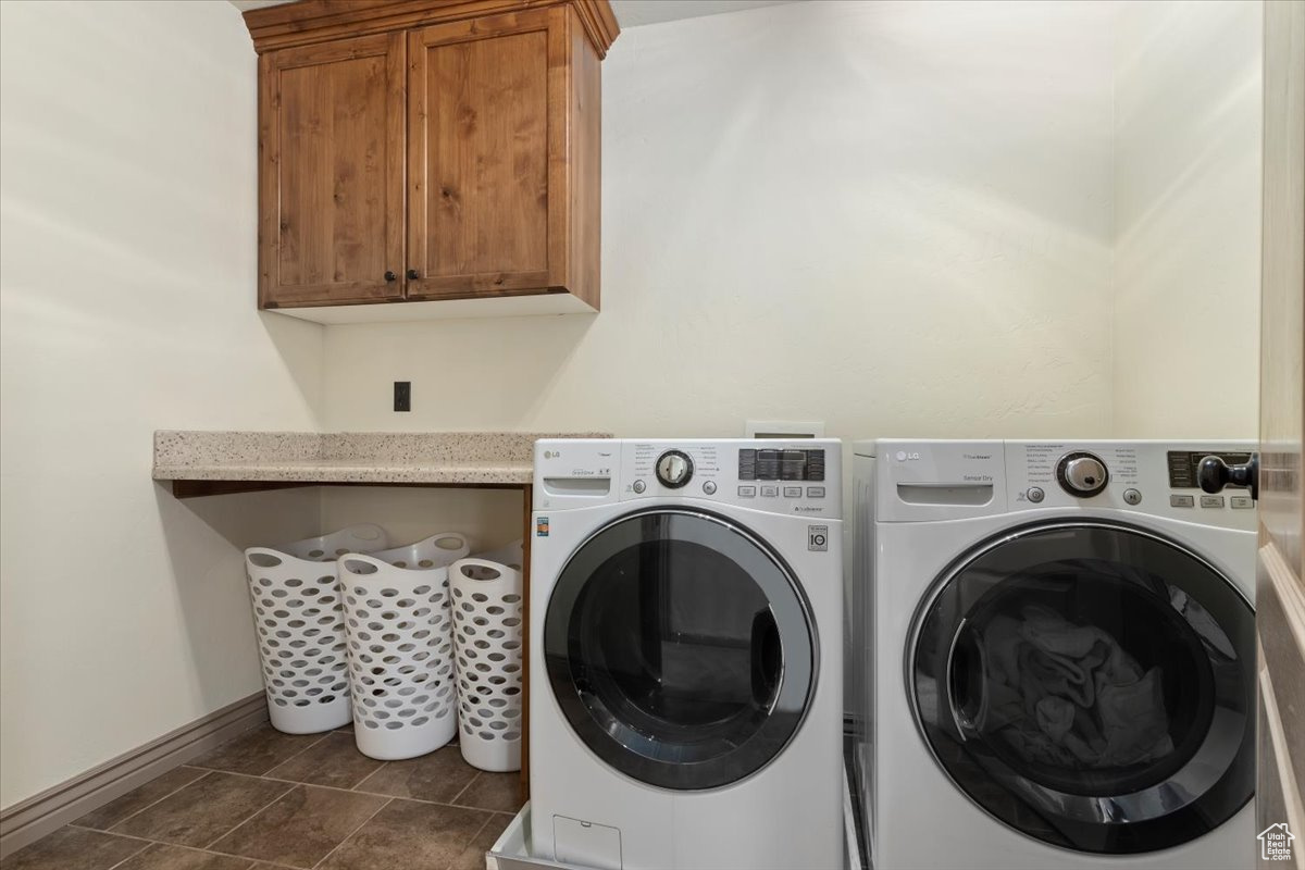 Washroom featuring cabinets, dark tile patterned flooring, and washing machine and dryer