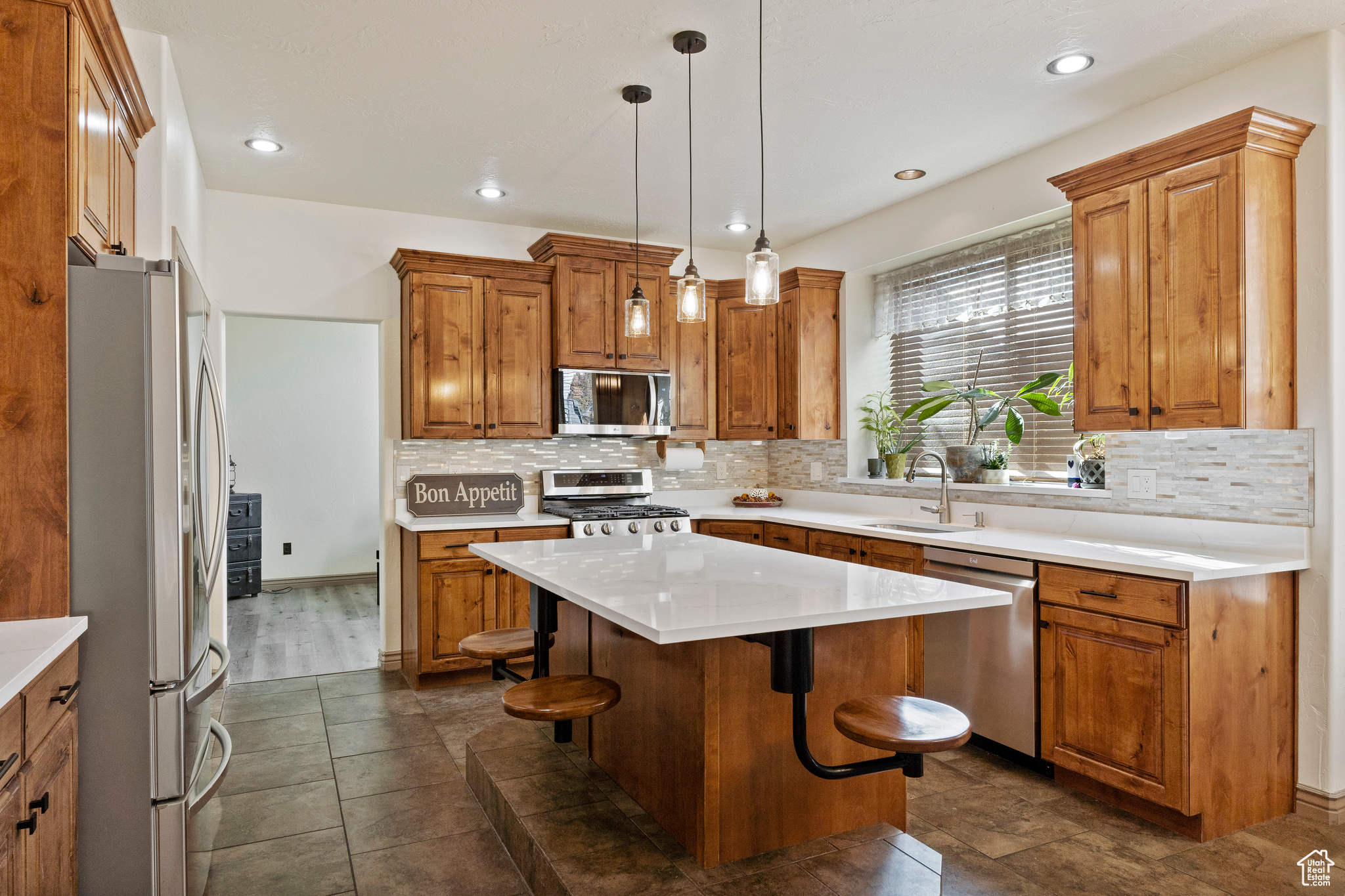 Kitchen with NEW appliances with stainless steel finishes, NEW backsplash, decorative light fixtures, a kitchen island, and a breakfast bar area with NEW quartz countertops