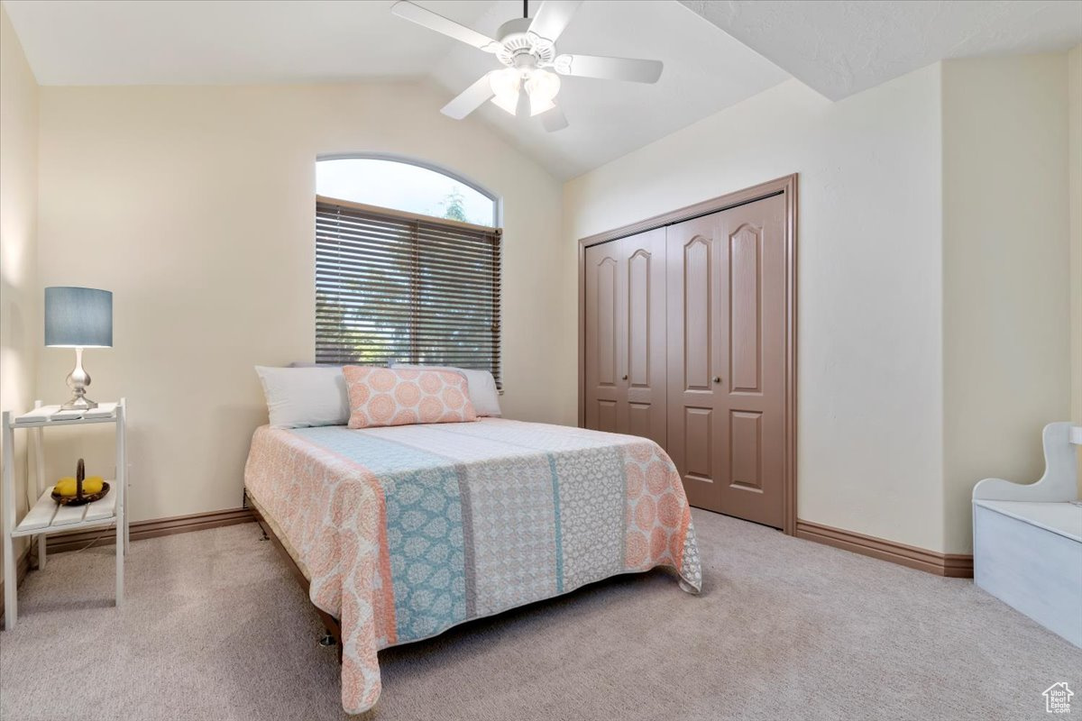 Carpeted bedroom featuring ceiling fan, a closet, and vaulted ceiling