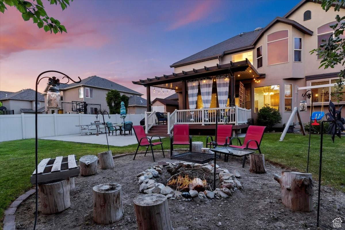 Patio terrace at dusk featuring a fire pit, a wooden deck, and a yard