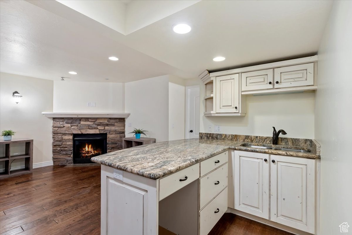 Kitchen with light stone counters, dark hardwood / wood-style floors, sink, kitchen peninsula, and a fireplace