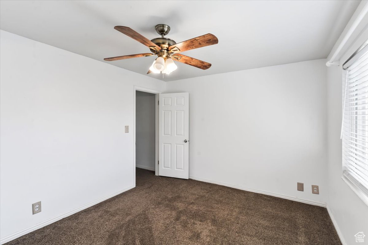 Unfurnished bedroom featuring ceiling fan, dark carpet, and multiple windows