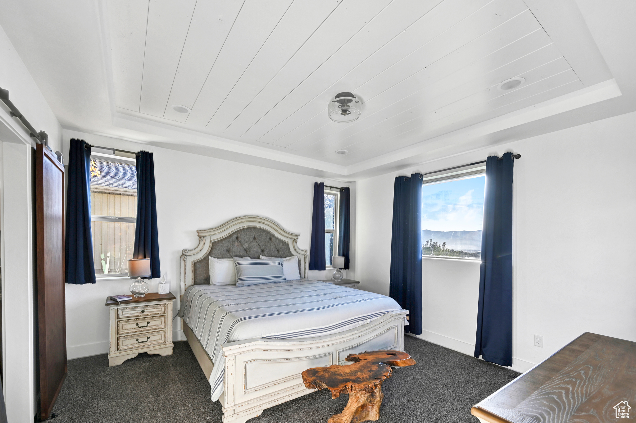 Bedroom with a raised ceiling, dark carpet, and a barn door