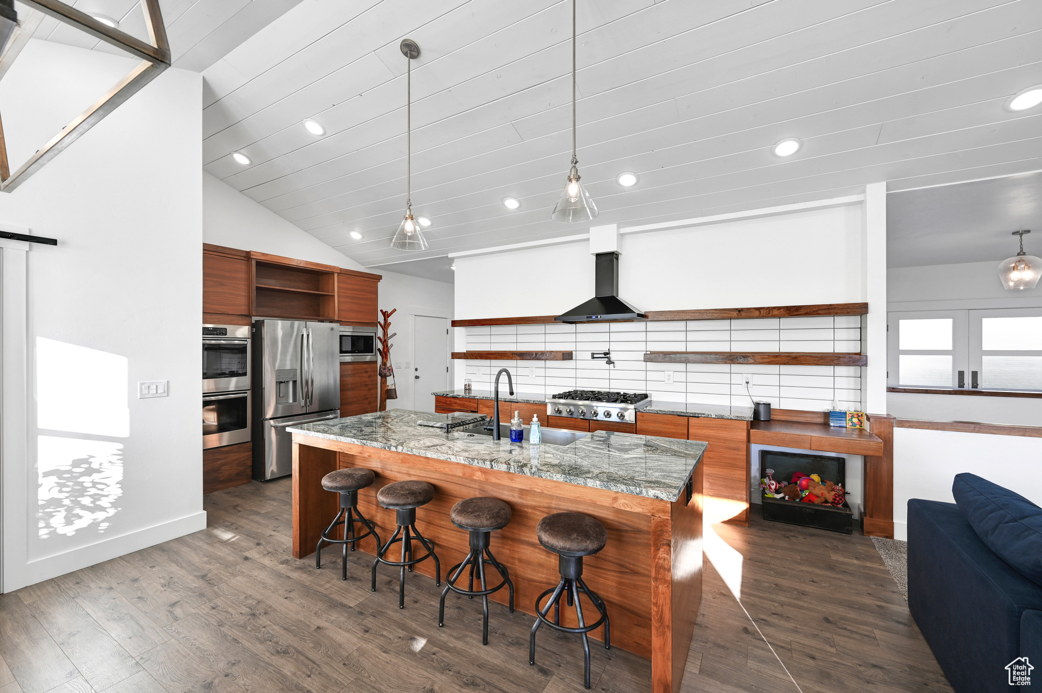 Kitchen with wall chimney exhaust hood, dark hardwood / wood-style floors, sink, hanging light fixtures, and appliances with stainless steel finishes