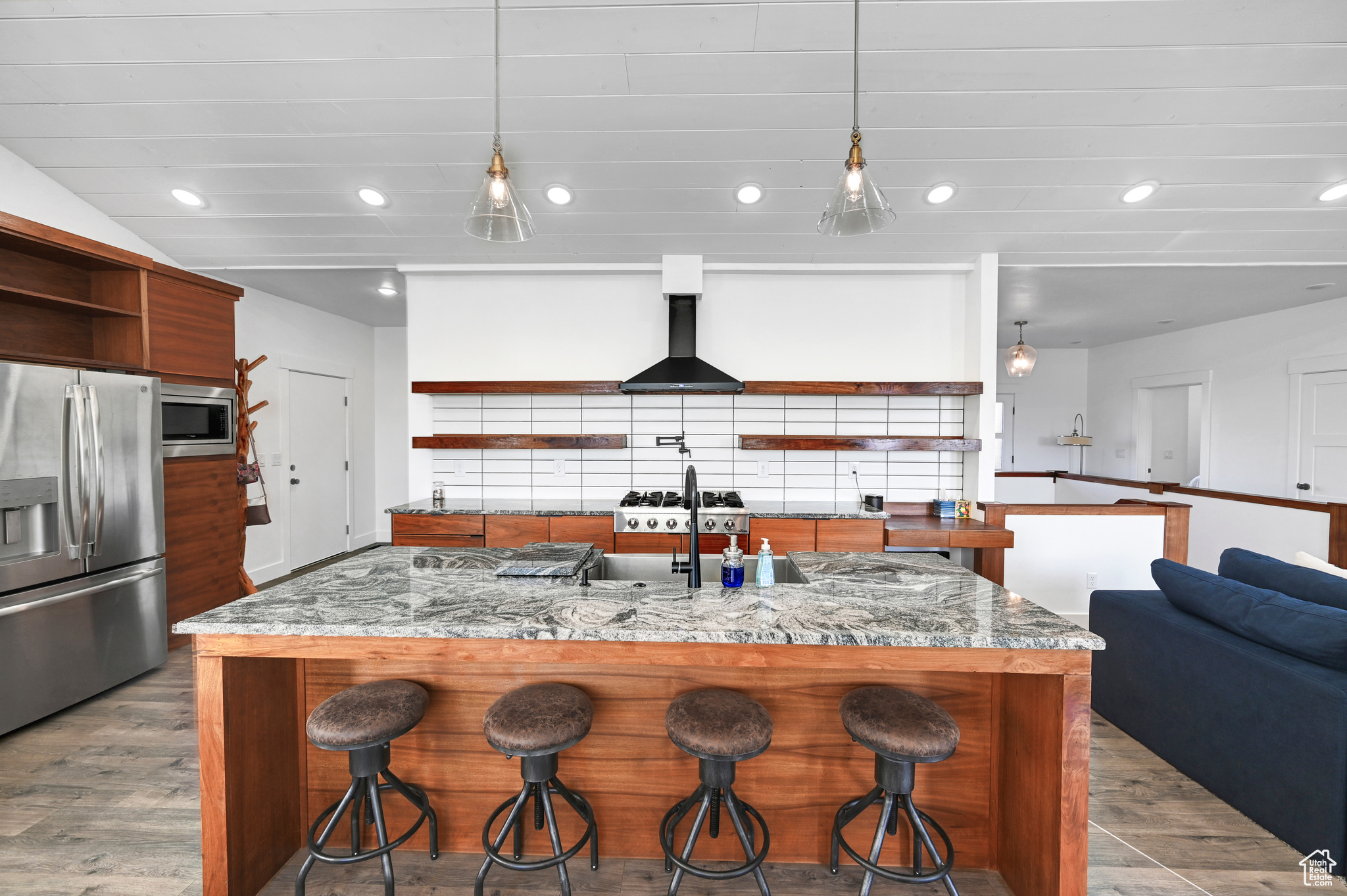 Kitchen with light stone counters, a kitchen island with sink, hardwood / wood-style flooring, appliances with stainless steel finishes, and range hood