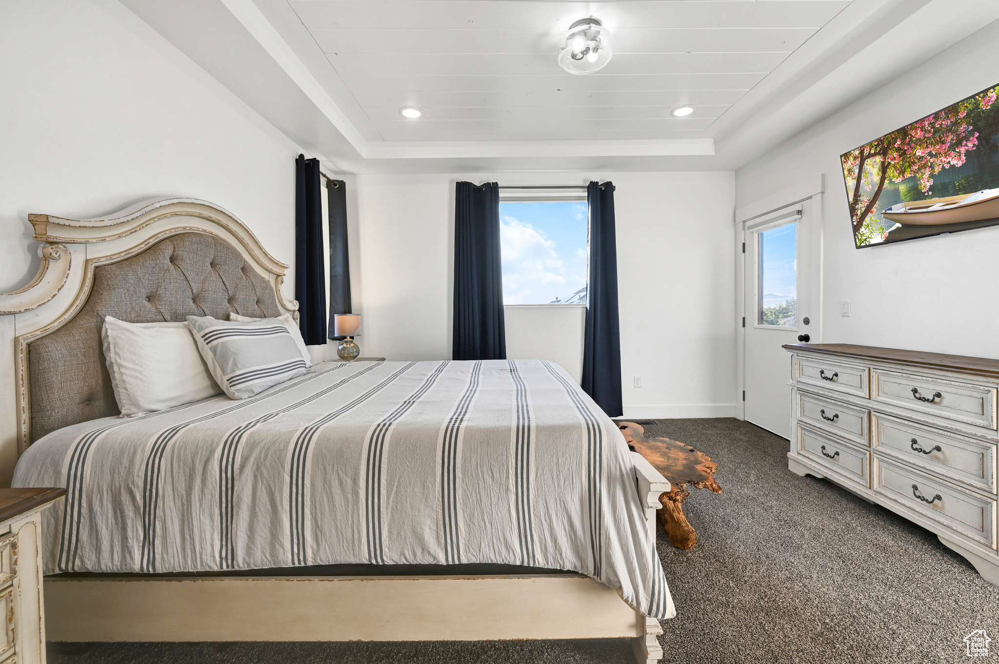 Bedroom with a tray ceiling, dark colored carpet, and multiple windows