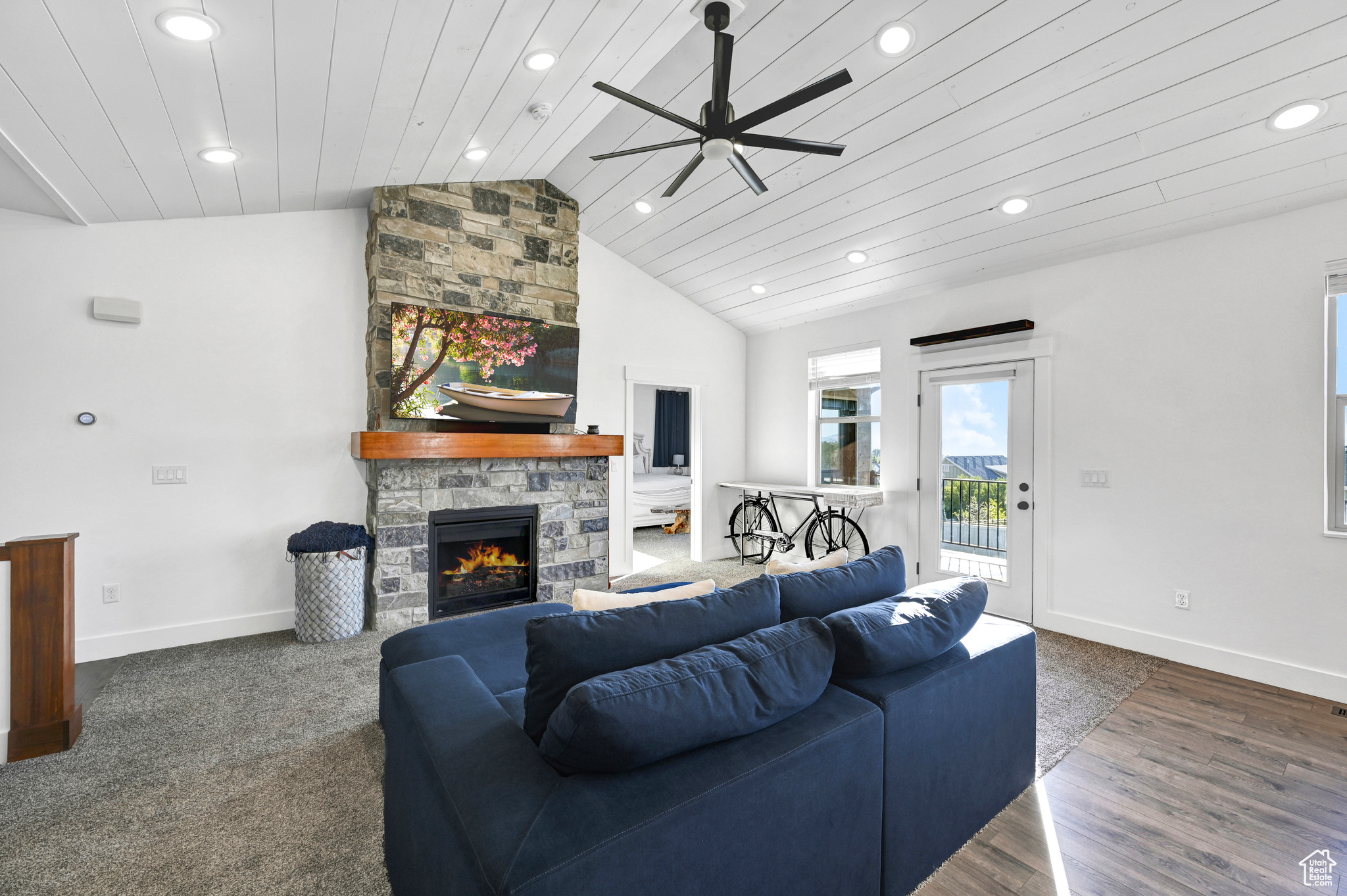 Living room with ceiling fan, a stone fireplace, wooden ceiling, vaulted ceiling, and dark hardwood / wood-style flooring