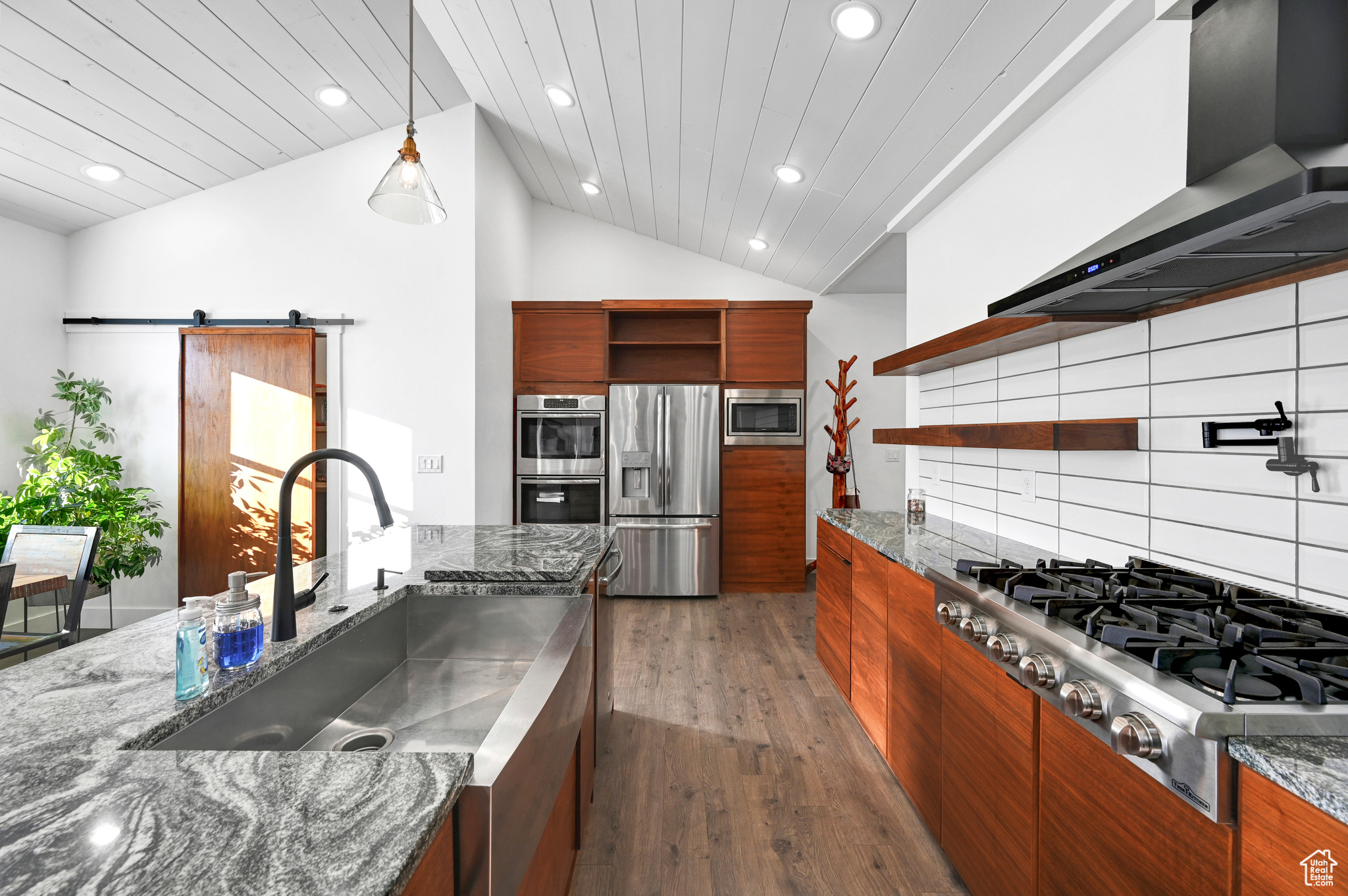 Kitchen featuring lofted ceiling, sink, wall chimney range hood, a barn door, and appliances with stainless steel finishes