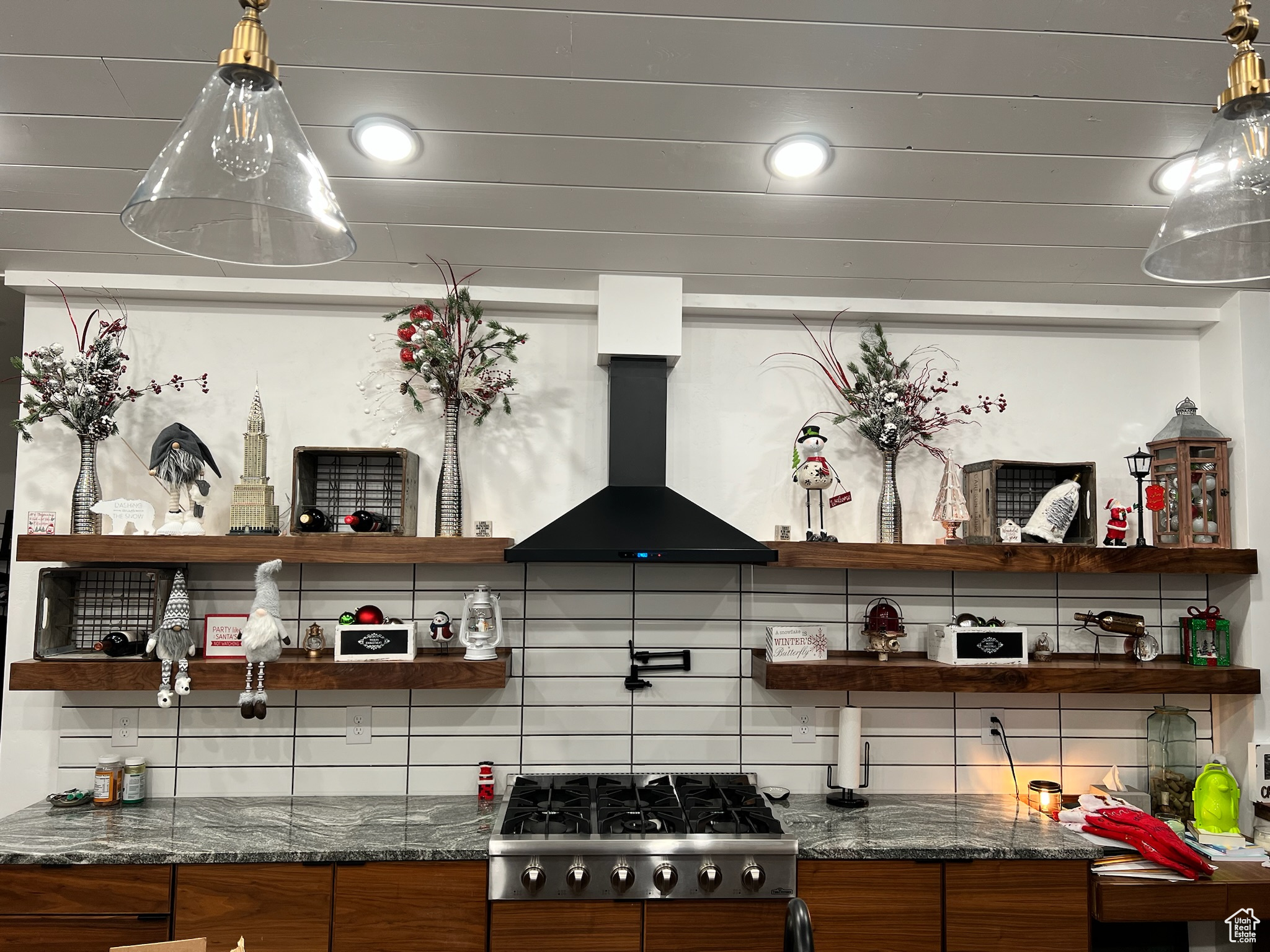 Kitchen featuring dark stone countertops, wall chimney range hood, stainless steel gas stovetop, and backsplash