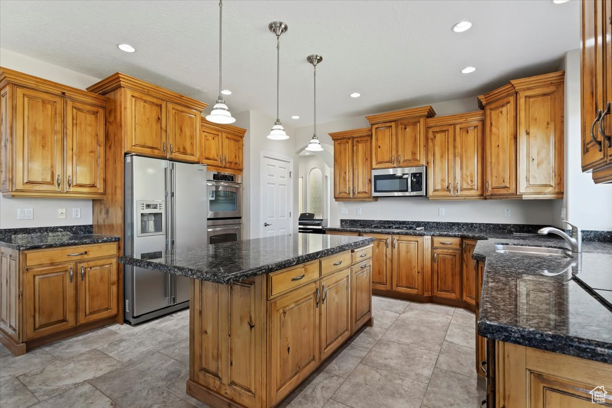 Kitchen with pendant lighting, sink, appliances with stainless steel finishes, a center island, and dark stone counters