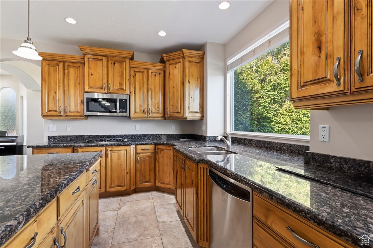 Kitchen with light tile patterned flooring, pendant lighting, dark stone counters, sink, and stainless steel appliances