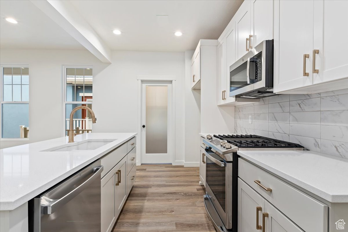 Kitchen featuring white cabinetry, sink, stainless steel appliances, tasteful backsplash, and light hardwood / wood-style flooring