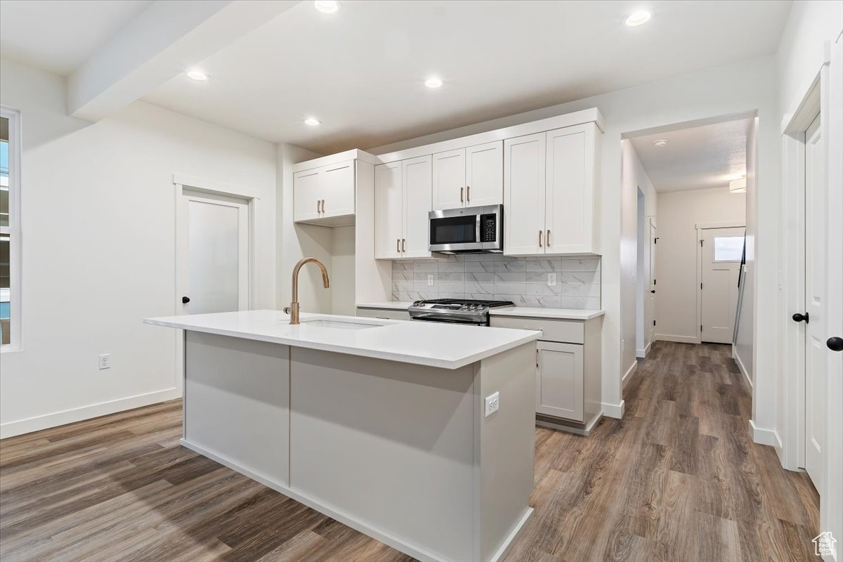 Kitchen with a kitchen island with sink, wood-type flooring, sink, white cabinetry, and stainless steel appliances