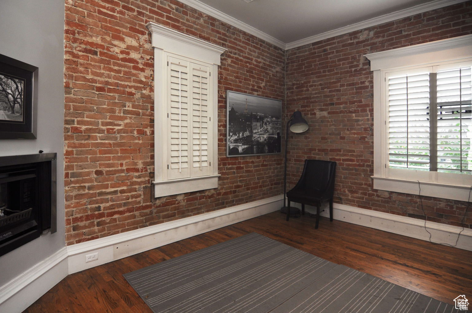 Unfurnished room featuring brick wall, crown molding, and dark hardwood / wood-style flooring