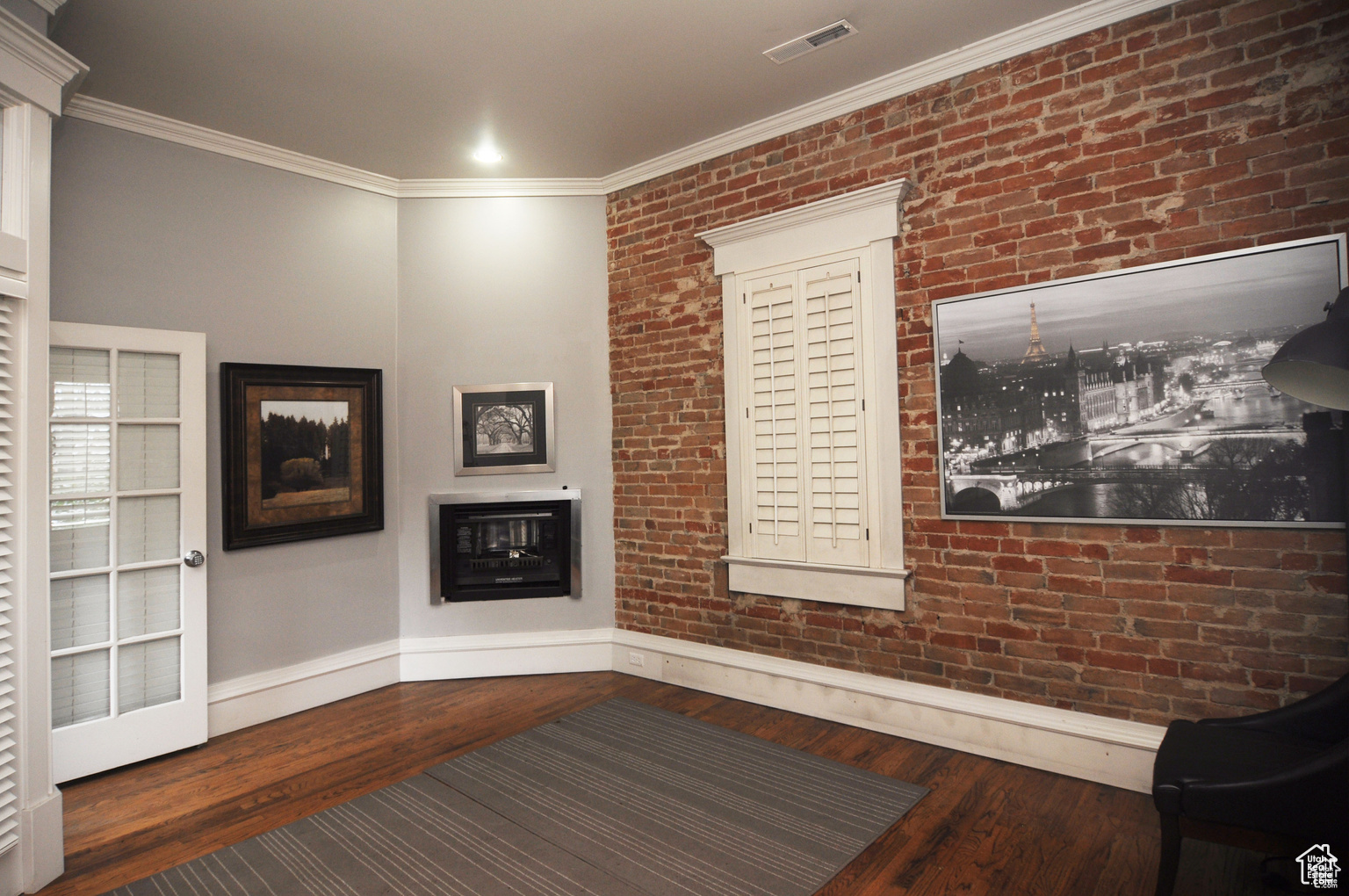 Interior space with dark wood-type flooring, ornamental molding, and brick wall