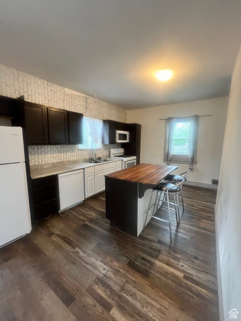 Kitchen featuring sink, white appliances, dark hardwood / wood-style floors, a breakfast bar area, and wood counters