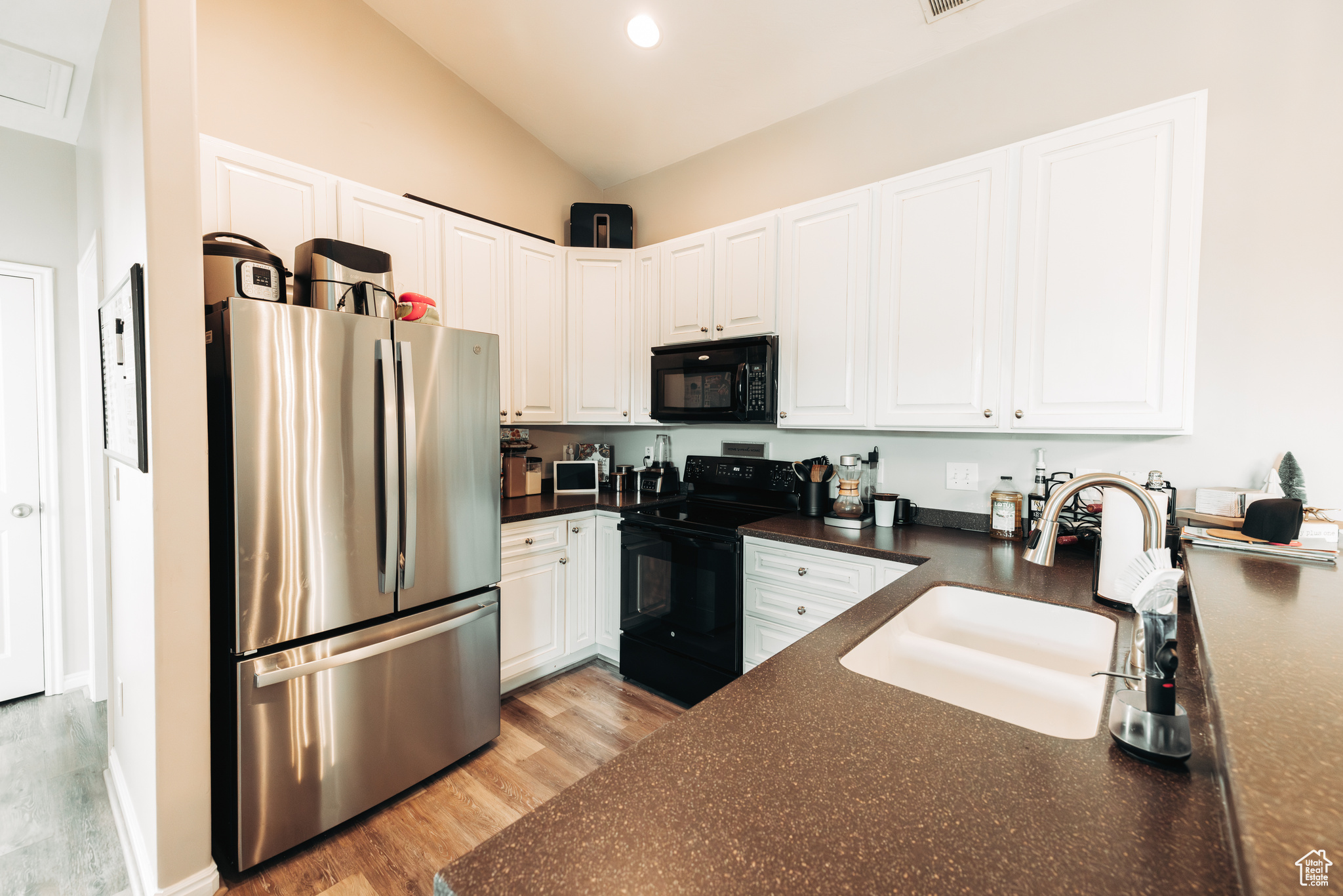 Kitchen with light hardwood / wood-style flooring, sink, lofted ceiling, black appliances, and white cabinetry