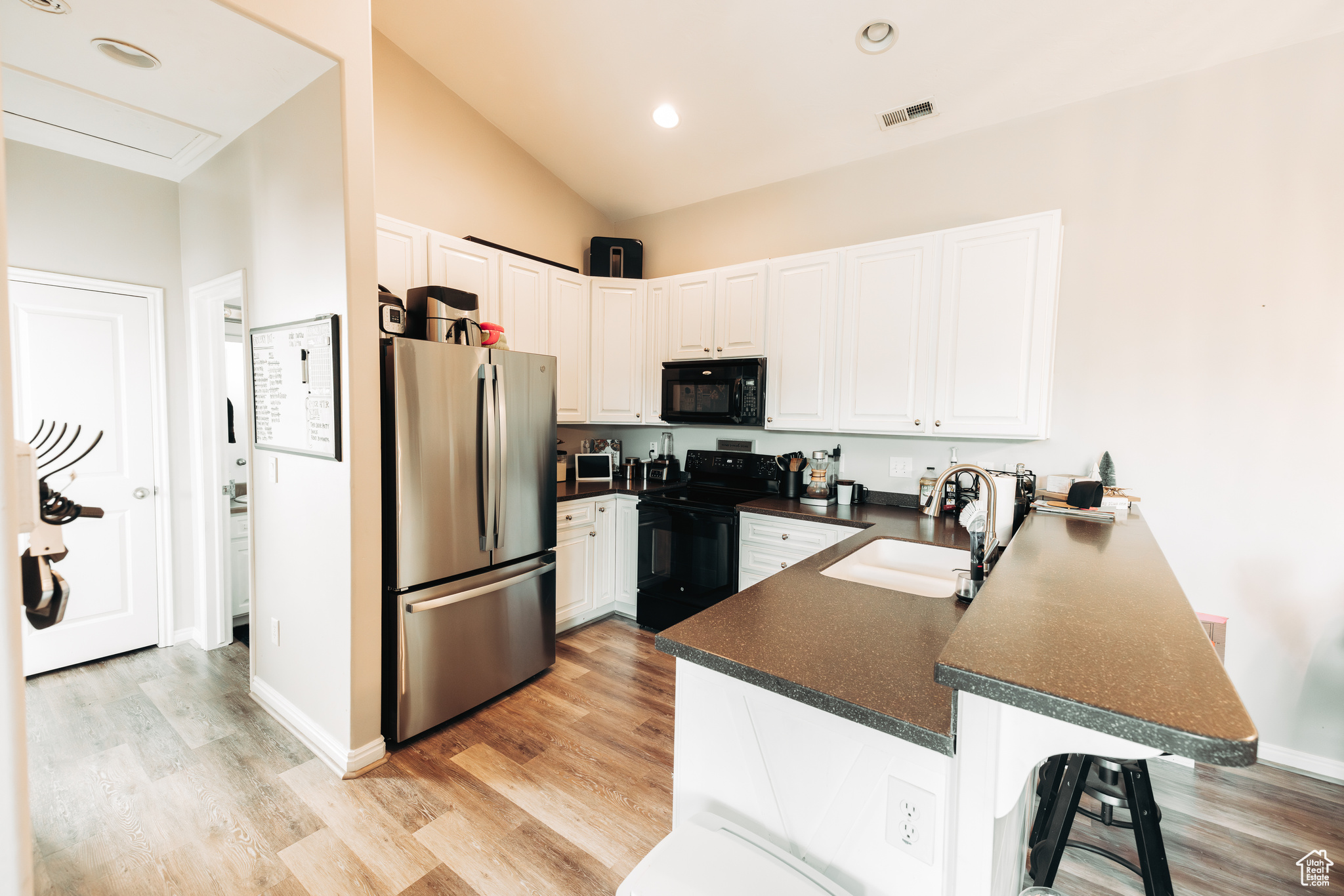 Kitchen featuring sink, kitchen peninsula, black appliances, a kitchen bar, and white cabinetry