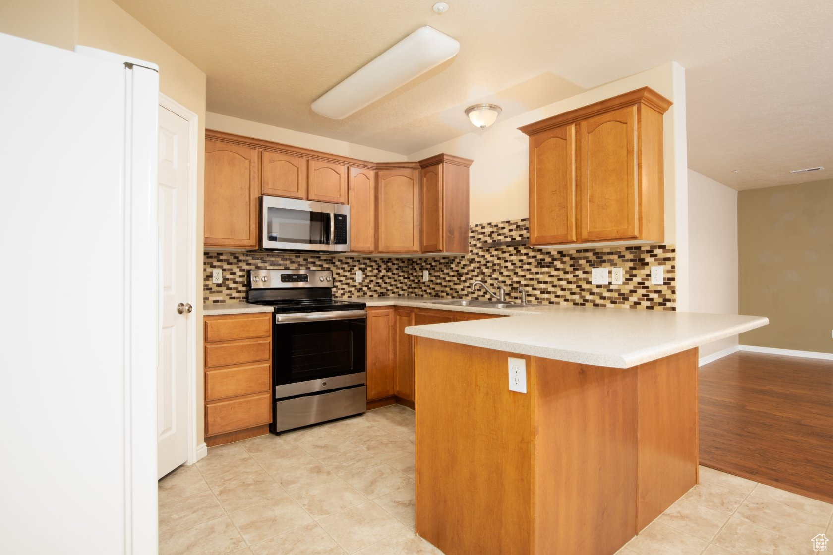 Kitchen featuring light wood-type flooring, tasteful backsplash, sink, kitchen peninsula, and appliances with stainless steel finishes