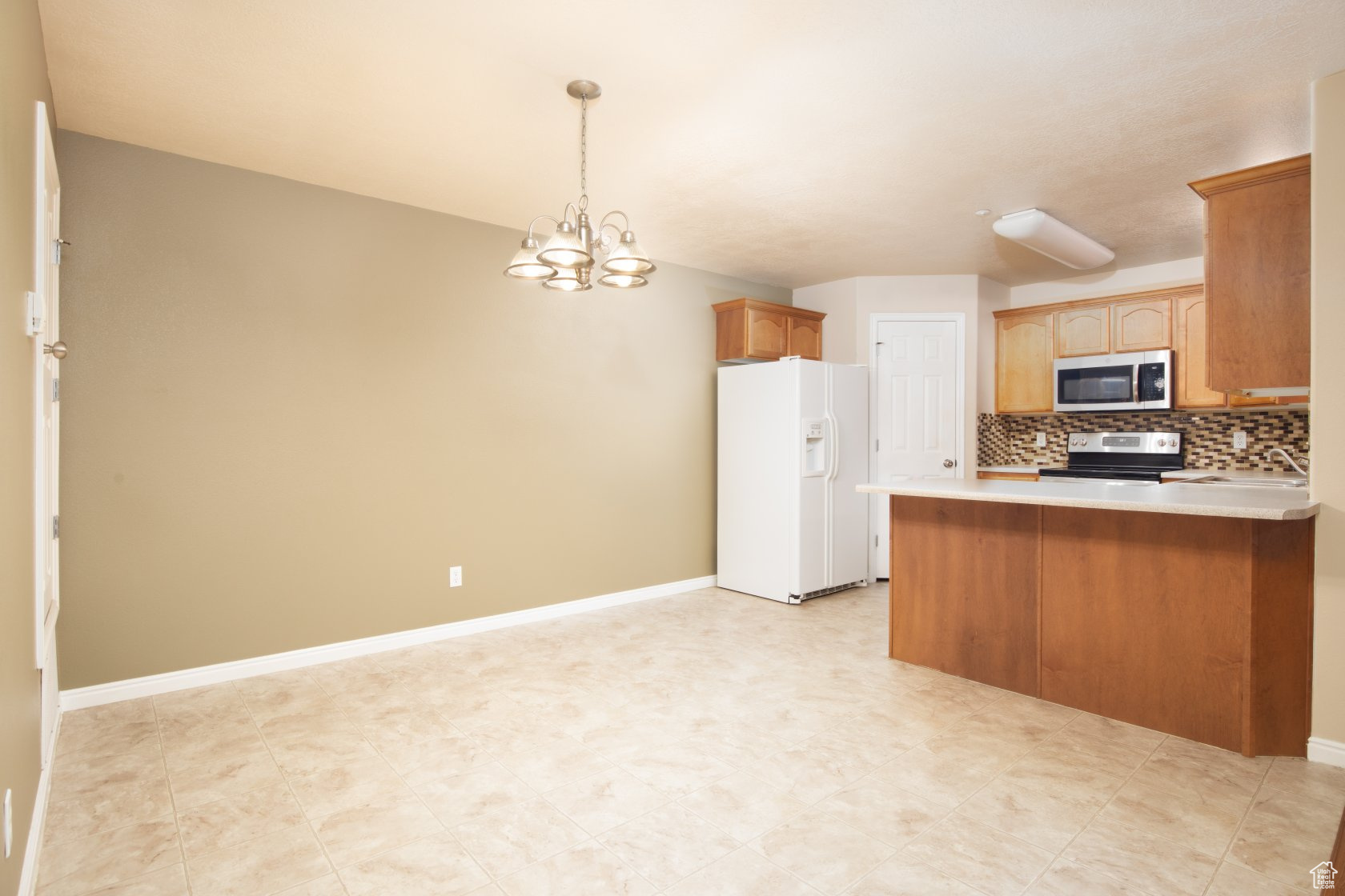 Kitchen with a chandelier, tasteful backsplash, decorative light fixtures, stainless steel appliances, and kitchen peninsula