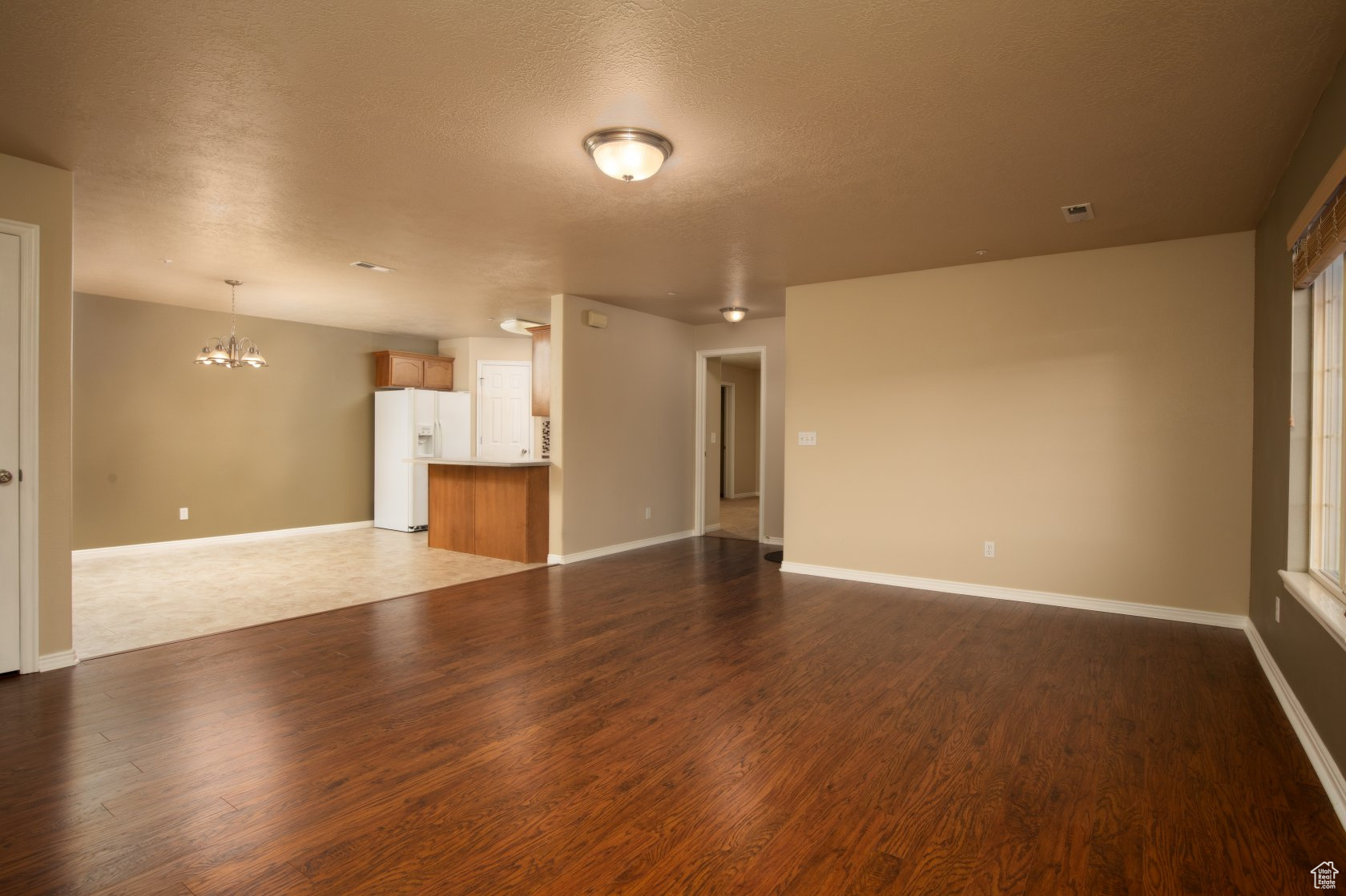 Unfurnished living room featuring an inviting chandelier, dark wood-type flooring, and a textured ceiling