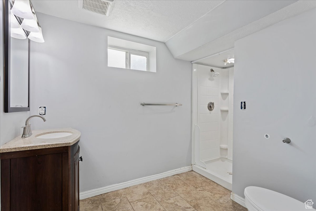 Bathroom featuring walk in shower, vanity, toilet, and a textured ceiling