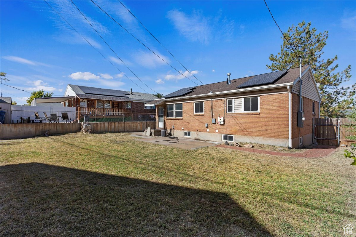 Back of property with a yard, a patio area, and solar panels