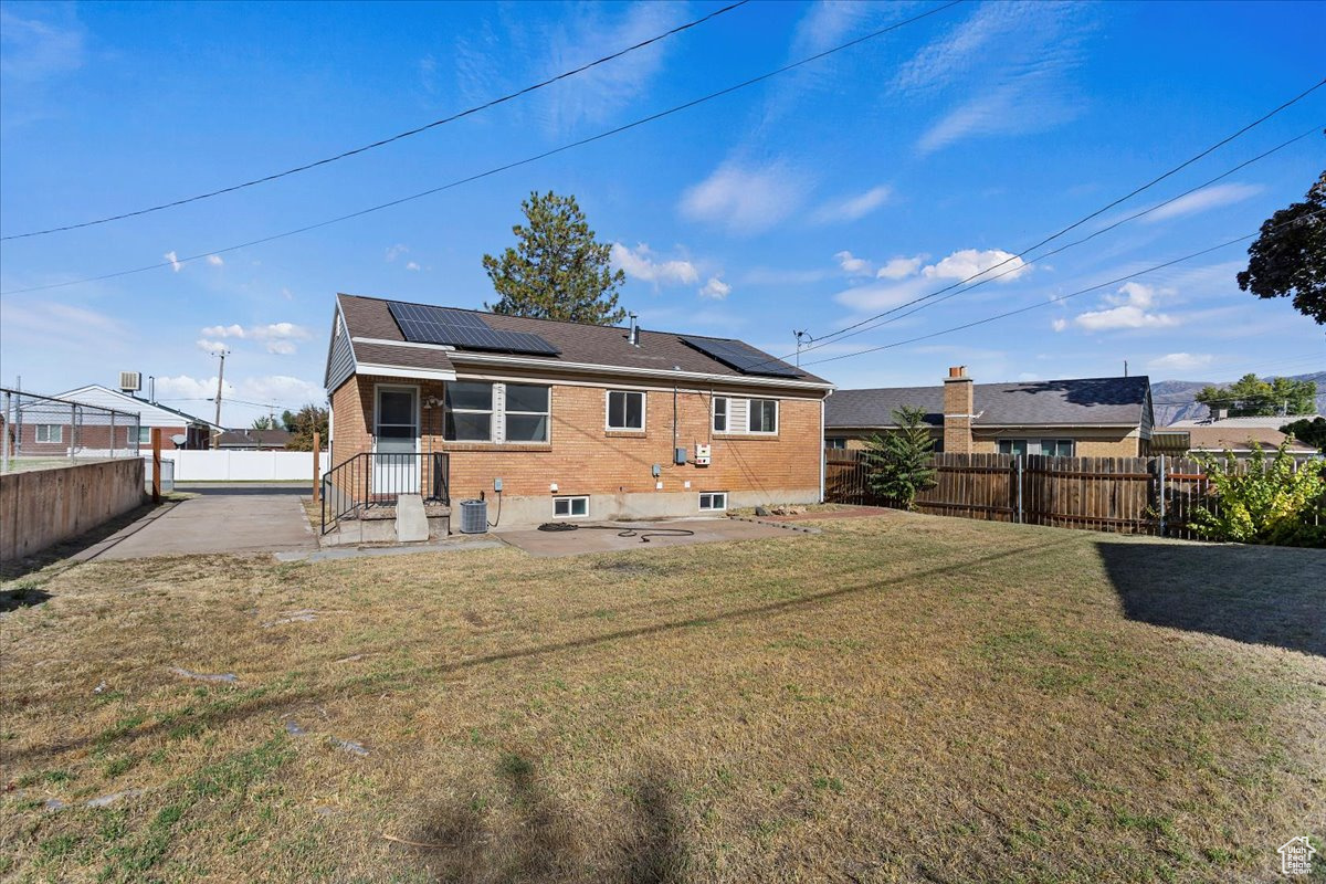 Rear view of house with a patio, a lawn, and solar panels