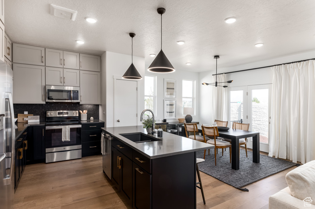 Kitchen with hanging light fixtures, sink, a center island with sink, stainless steel appliances, and hardwood / wood-style floors