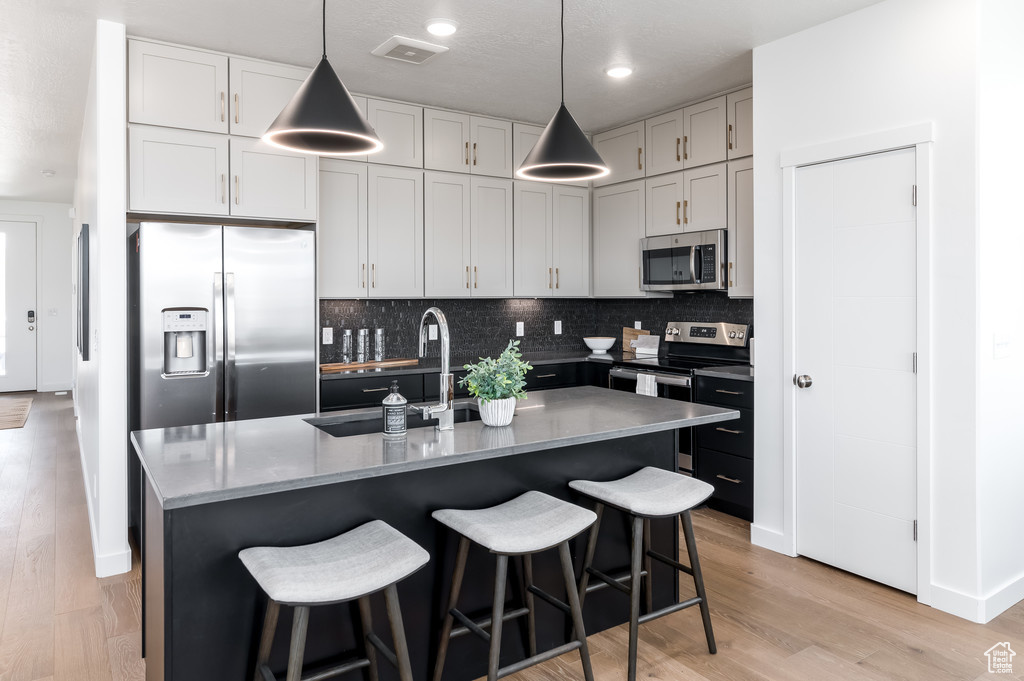 Kitchen with light stone counters, pendant lighting, sink, light hardwood / wood-style flooring, and appliances with stainless steel finishes