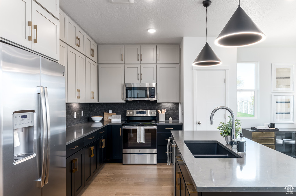 Kitchen with an island with sink, stainless steel appliances, sink, pendant lighting, and dark stone counters