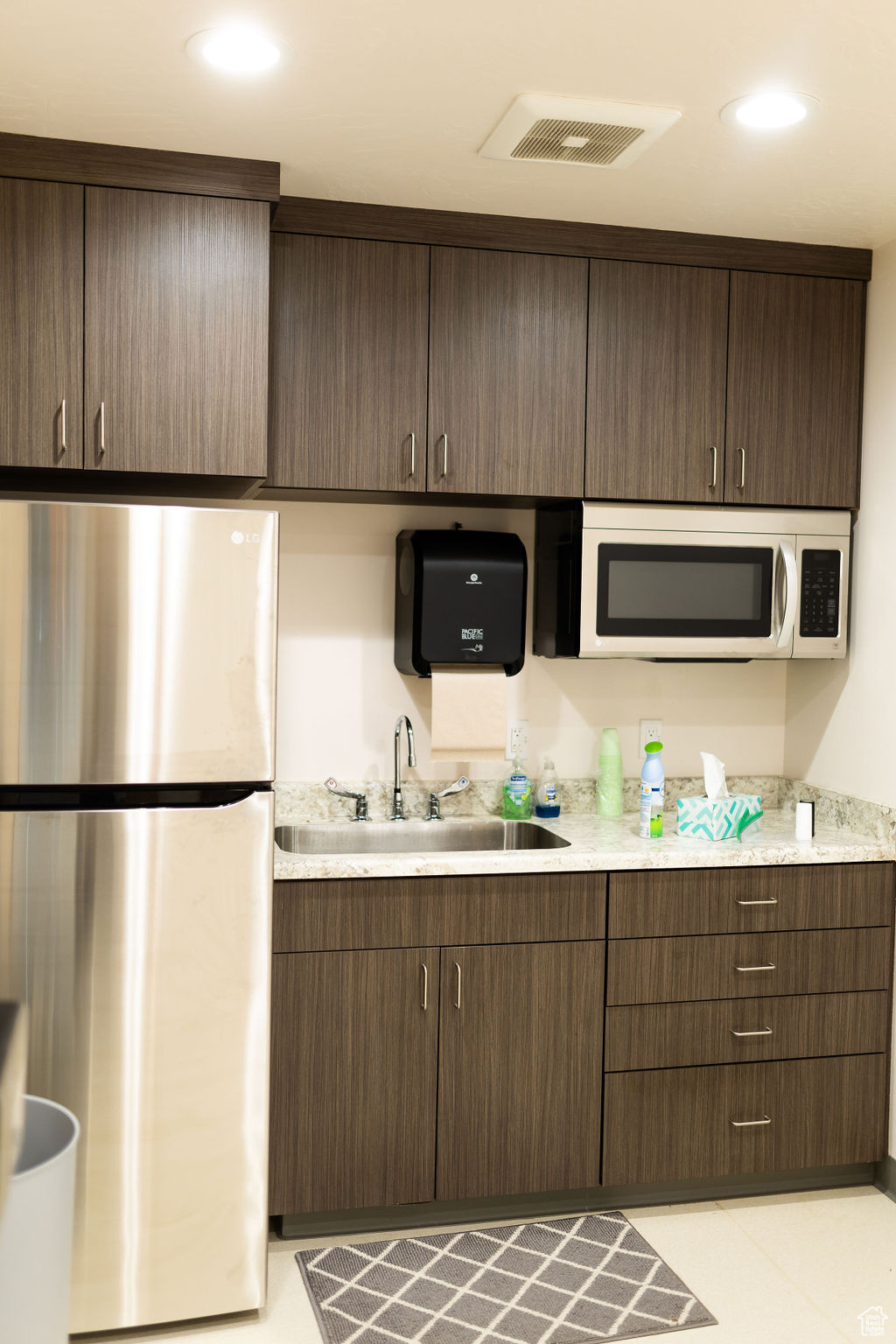 Kitchen featuring sink, stainless steel fridge, light stone counters, and dark brown cabinets