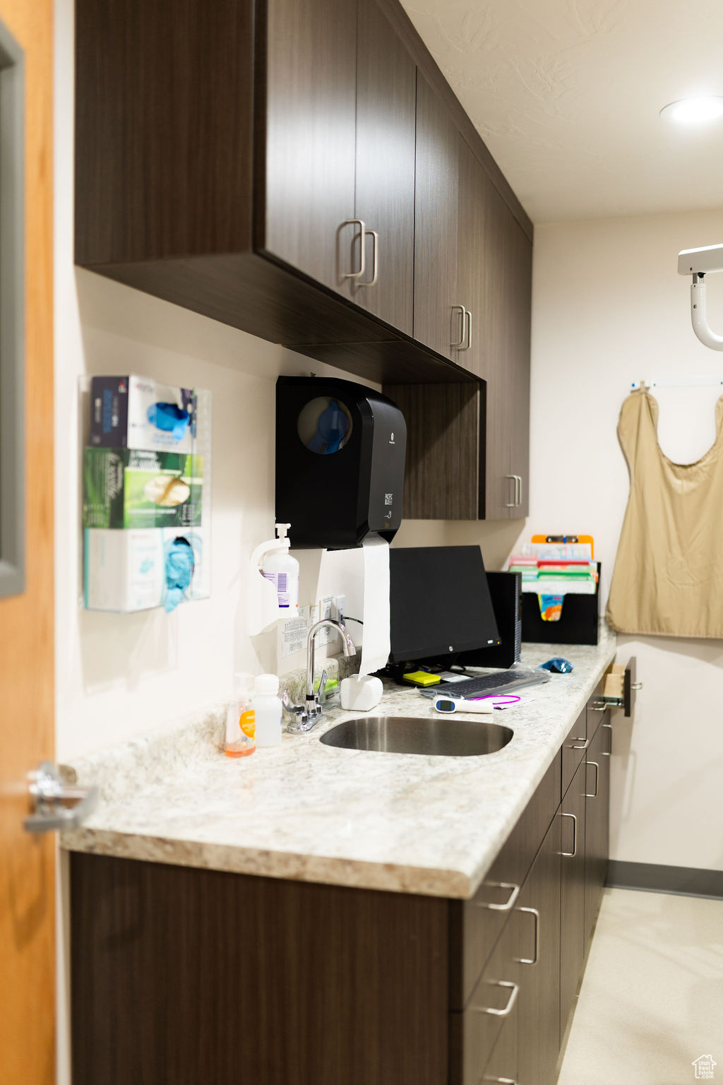 Kitchen featuring light stone counters, dark brown cabinets, and sink