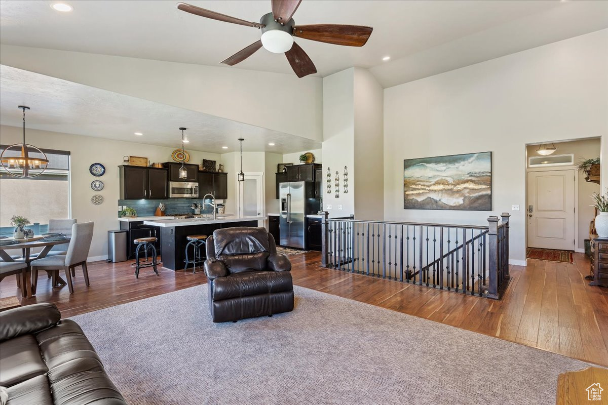 Living room with ceiling fan with notable chandelier, high vaulted ceiling, dark hardwood / wood-style flooring, and sink