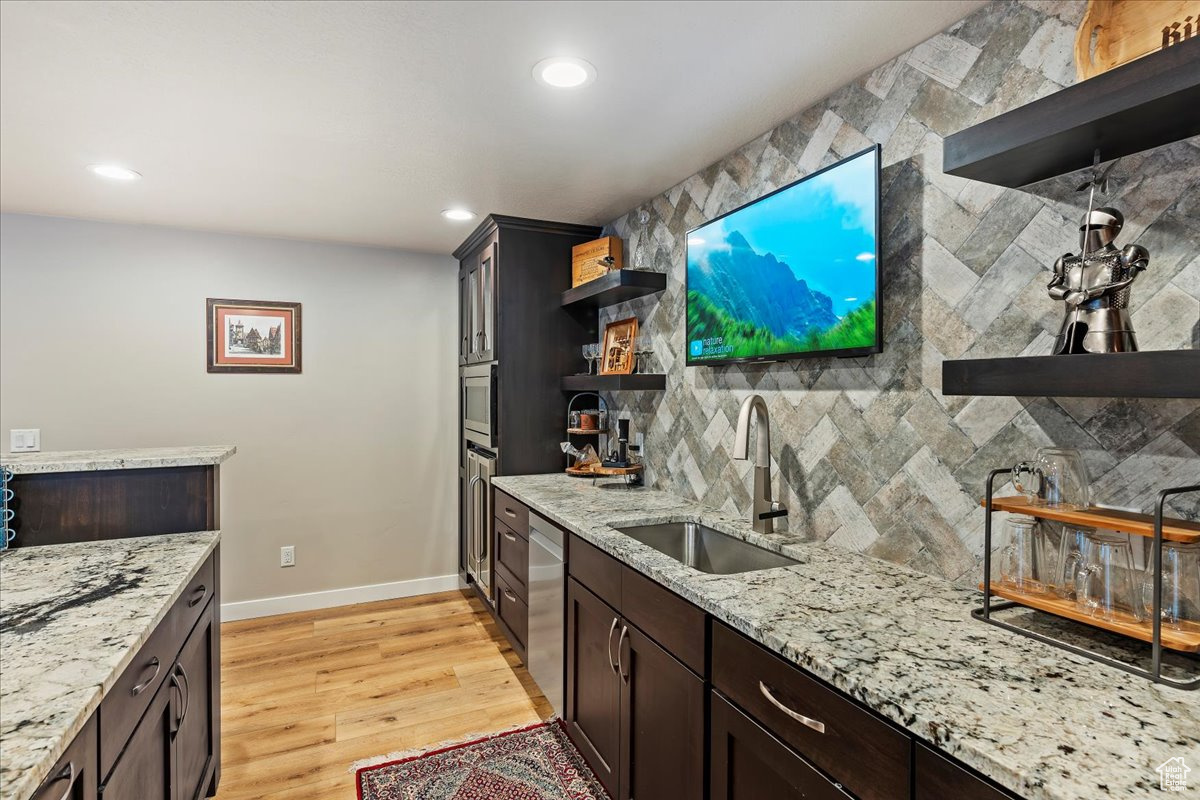 Kitchen with light stone counters, dark brown cabinetry, sink, light hardwood / wood-style floors, and dishwasher