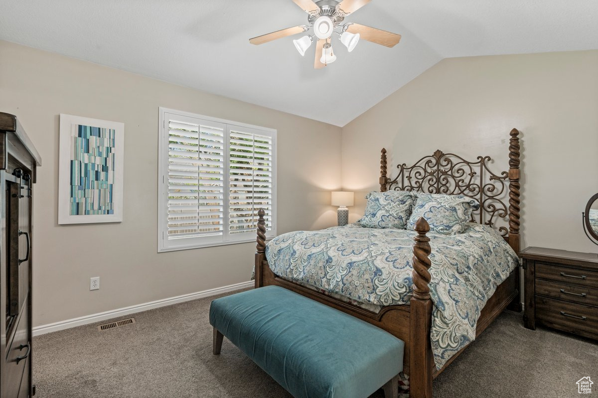 Carpeted bedroom with ceiling fan and vaulted ceiling