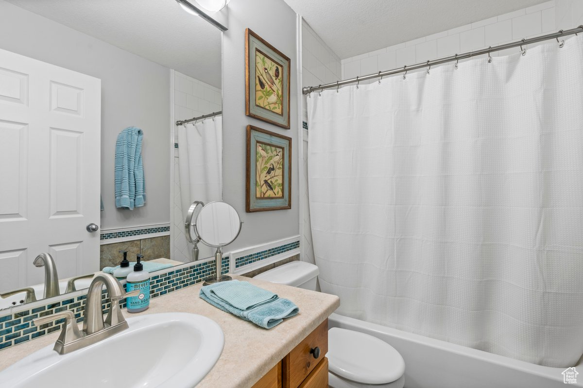 Full bathroom featuring vanity, toilet, shower / bathtub combination with curtain, and decorative backsplash