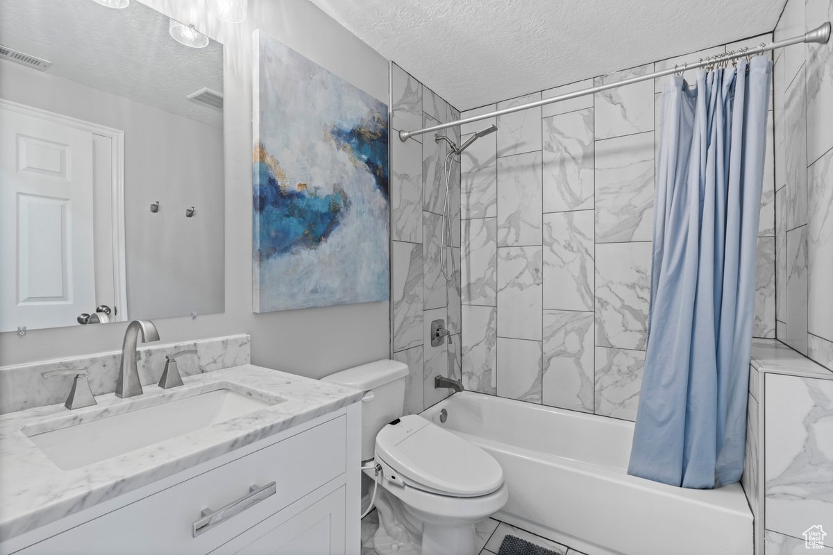 Full bathroom with shower / bath combination with curtain, vanity, toilet, and a textured ceiling