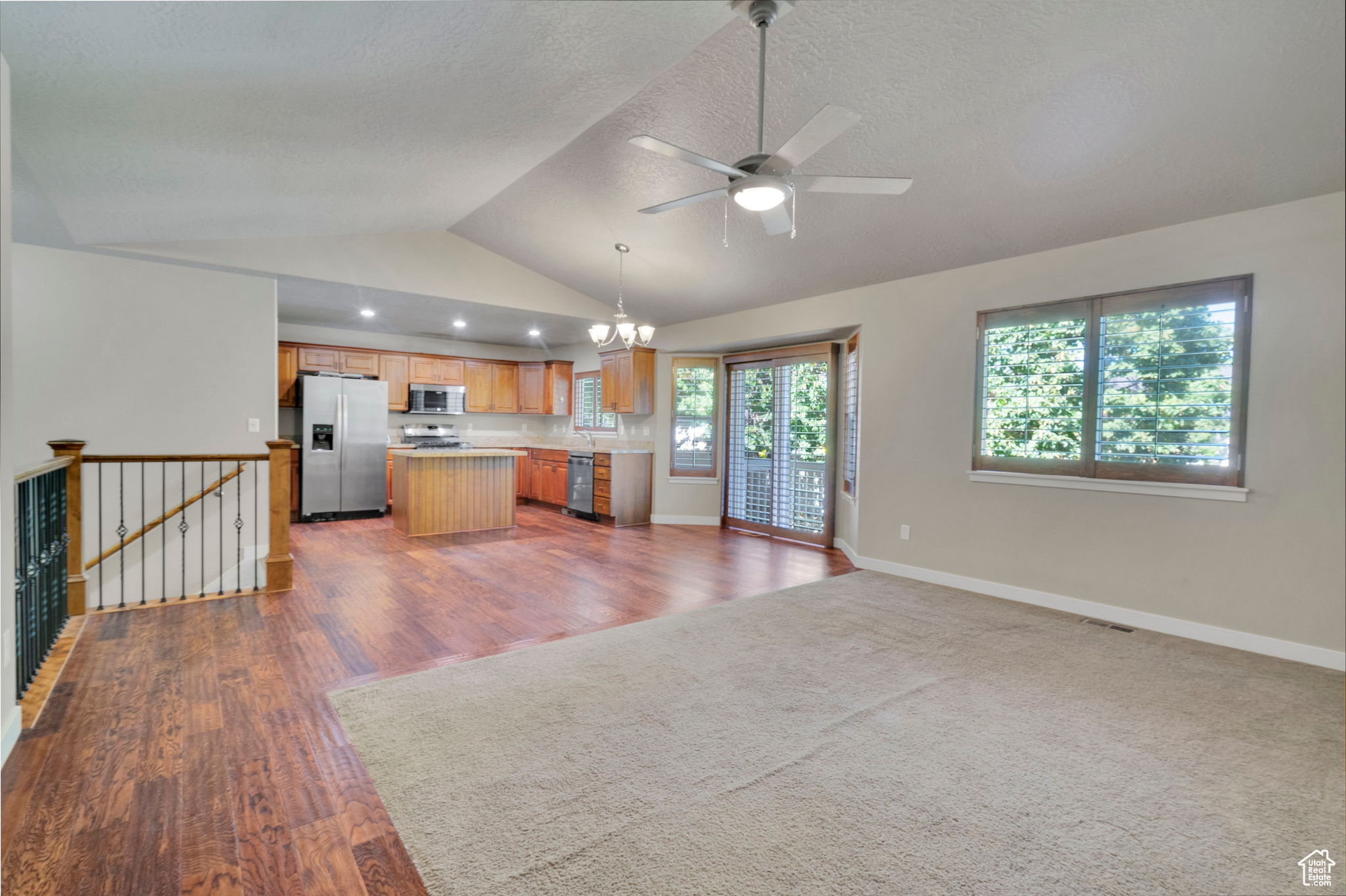 Kitchen featuring dark wood-type flooring, stainless steel appliances, a center island, vaulted ceiling, and decorative light fixtures