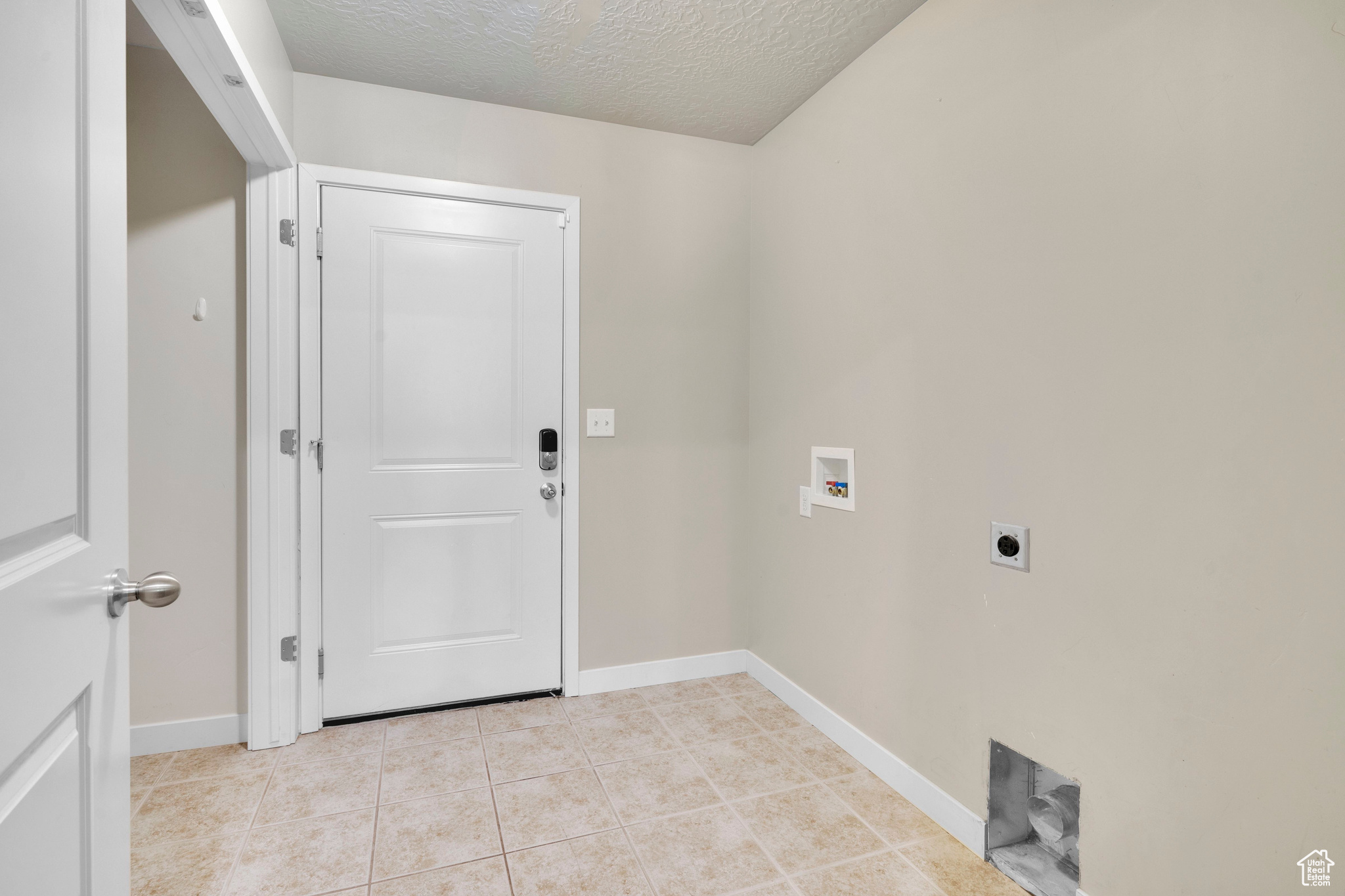 Clothes washing area with hookup for an electric dryer, a textured ceiling, washer hookup, and light tile patterned floors