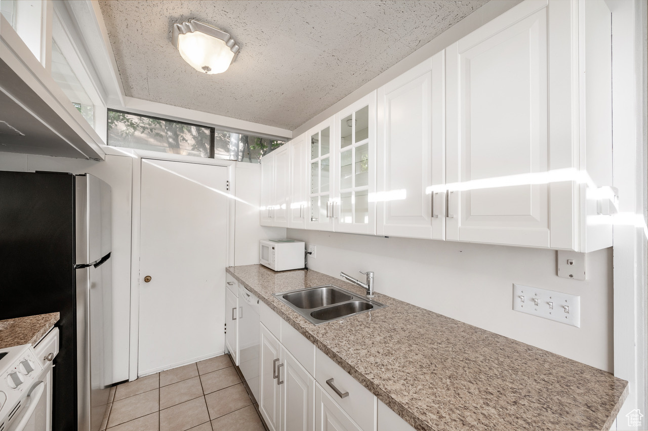 Kitchen featuring white appliances, white cabinetry, sink, light tile patterned floors, and a textured ceiling