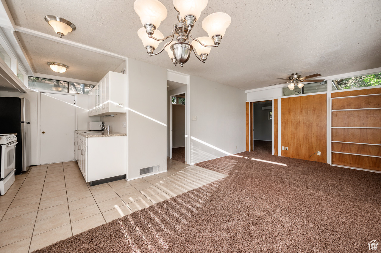 Kitchen with ceiling fan with notable chandelier, white electric range oven, white cabinetry, and a textured ceiling