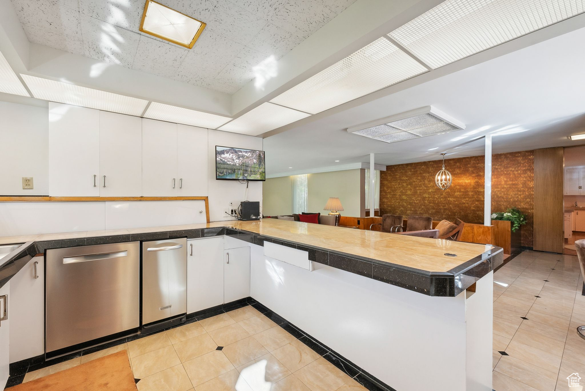 Kitchen with dishwasher, a kitchen breakfast bar, kitchen peninsula, light tile patterned flooring, and white cabinetry