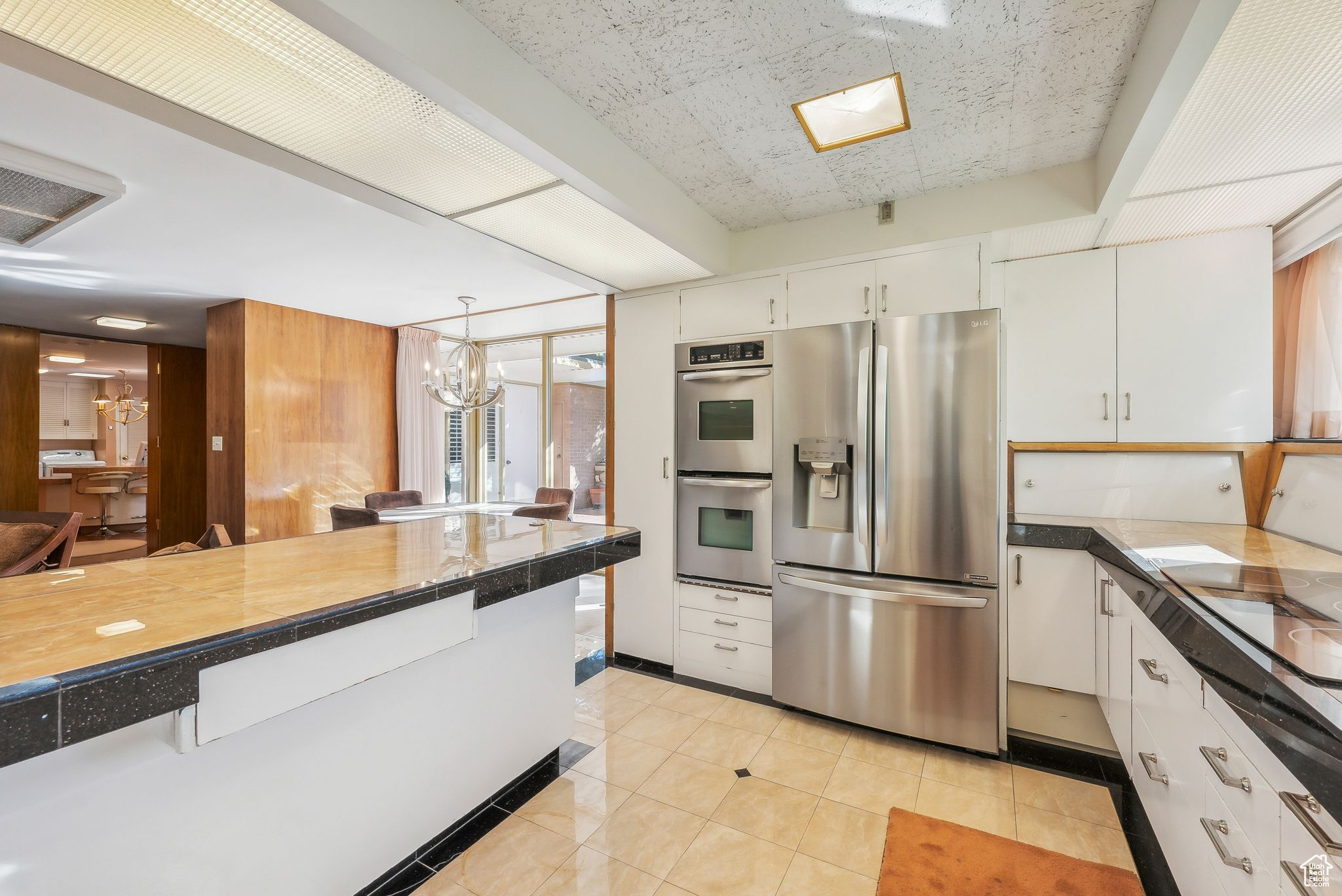 Kitchen with appliances with stainless steel finishes, light tile patterned flooring, hanging light fixtures, white cabinetry, and a chandelier