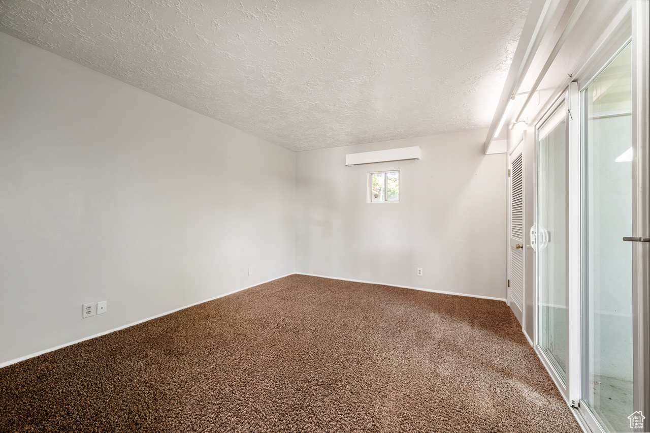 Carpeted spare room featuring a textured ceiling and an AC wall unit