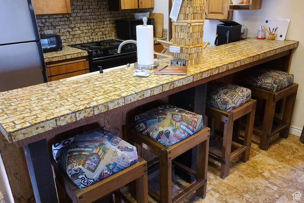 Kitchen featuring a breakfast bar, kitchen peninsula, black range with gas cooktop, and decorative backsplash