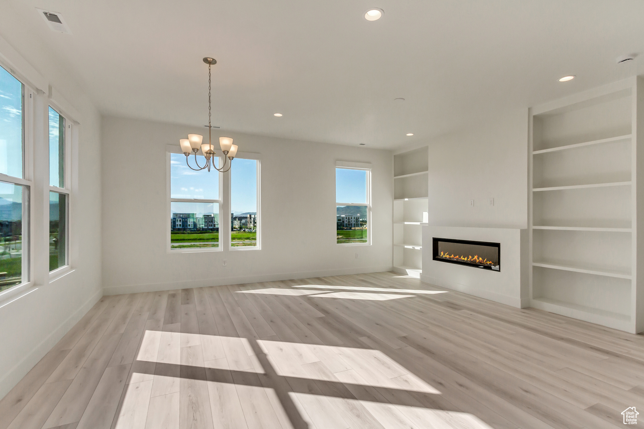 Unfurnished living room with a notable chandelier, built in features, and light hardwood / wood-style flooring