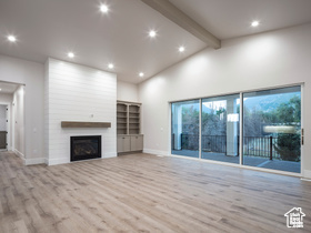 Unfurnished living room featuring beam ceiling, high vaulted ceiling, a fireplace, and light wood-type flooring