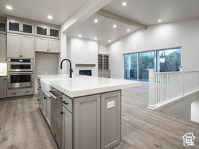 Kitchen featuring appliances with stainless steel finishes, light wood-type flooring, lofted ceiling with beams, gray cabinets, and a center island with sink